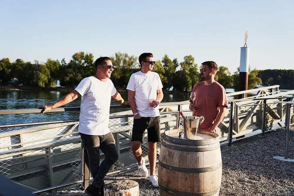 Drei Freunde mit Wein am Holzfass vor dem Rhein