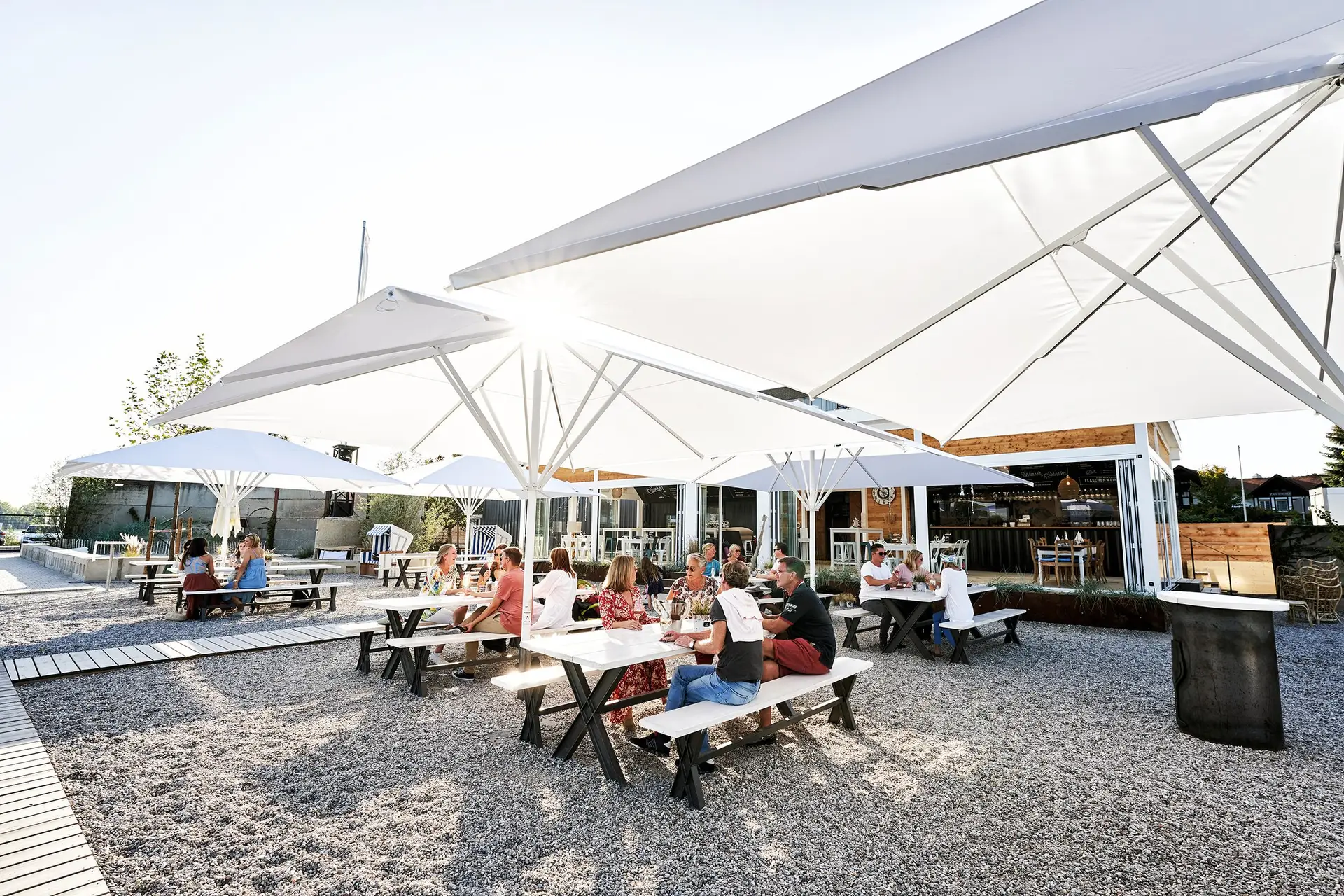 Gäste unter weißen Sonnenschirmen auf dem Kiesplatz von Allendorf am Rhein